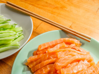 Selective focus on salmon and fresh cucumber slices on plates and bamboo chopsticks. Flat lay. Appetizing vibrant ingredients from Asian cuisine.