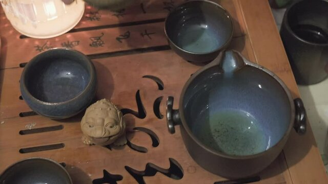 Camera moves along the tea board shooting close up. Man hand pours green tea over a clay frog figurine. The concept of Chinese and Japanese tea ceremonies, hobbies and lifestyle