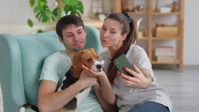 Couple take a selfie with dog on smartphone while sitting on sofa Spbi. Woman hold phone