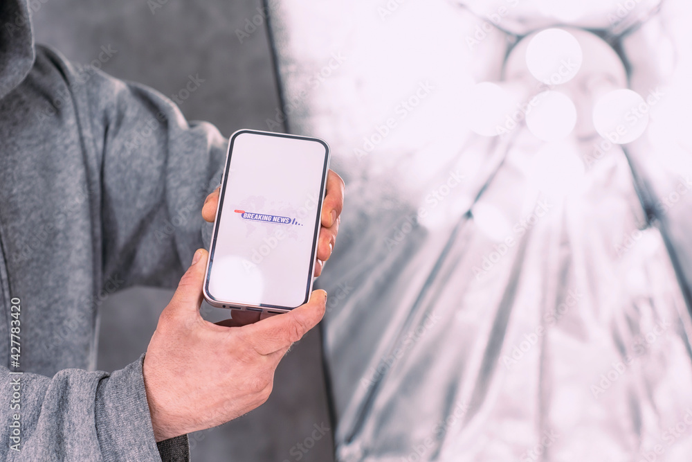Poster phone display with a breaking news icon set against a backdrop of studio lighting. a man holds a moc