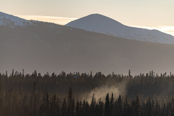 Silhouette of multiple layers of mountains and wilderness boreal forest in northern Canada at sunset with smoke pouring out of the woods below. 