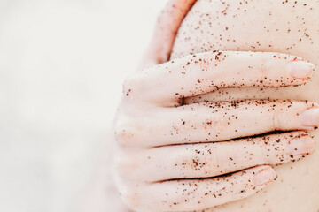 close up of a woman holding her arm applying coffee body scrub. home spa. me-time and relaxing beauty treatment. selective focus