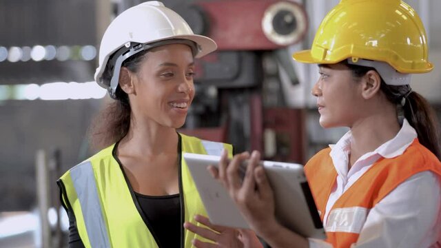 Two female engineers worker wearing protective uniform brainstorming and discuss project in industry manufacturing factory. woman using tablet device checking work, team colleague note on checklist.