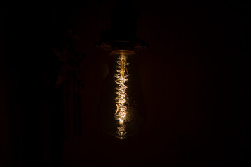 Incandescent bulb. Vintage hanging Edison light bulb over black background