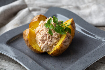 Jacket Potato , Baked Potato with Tuna mayonnaise on grey square plate on wooden background. Horizontal, side view