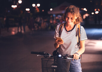 Beautiful happy smiling young woman using bike rental app in night european city