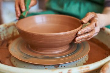 Close-up female hands working on a potter's wheel making bowl.