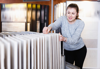 Young glad smiling female choosing kitchen ceramic tile in modern shop