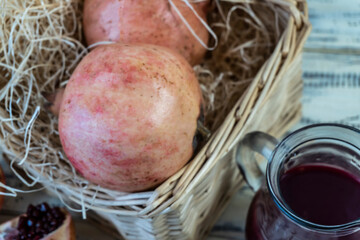 Pomegranates in a basket and on the table on a wooden background. Pomegranate juice in a jug and...