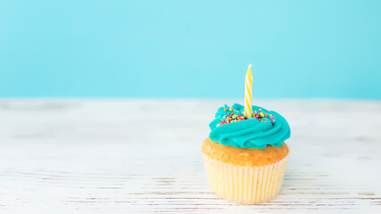 Birthday greeting concept. Yellow candle on muffin, cupcake. Blue background