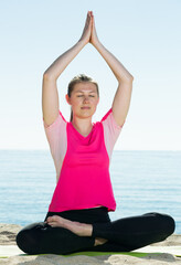 Fototapeta na wymiar Young woman exercising yoga poses on sunny beach by ocean