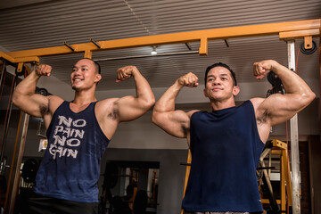Two friends enjoy a friendly posedown after training, doing double bicep poses. Having fun and...