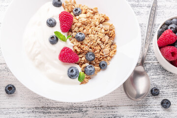 Yogurt with baked granola and berries in white ceramic plate on wooden background. Healthy breakfast. Copy space - Image