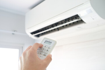 Man's hand using remote control open The air conditioner is cooled to 25 degrees Celsius in his bedroom. Health concepts and energy savings