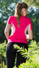 Athletic woman in pink T-shirt is jogging back in the park.