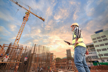 Civil engineer or architect with hardhat on construction site checking schedule on tablet...