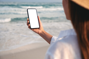 Mockup image of a woman holding mobile phone with blank desktop screen on the beach