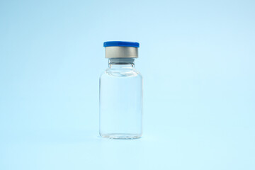 Obraz na płótnie Canvas A vaccine in a glass bottle on a light blue background. Vaccine for immunization, and treatment from virus infection. Side view. Concept of medical and healthcare