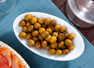 Oval dish with pickled olives with a stone on a blue napkin.