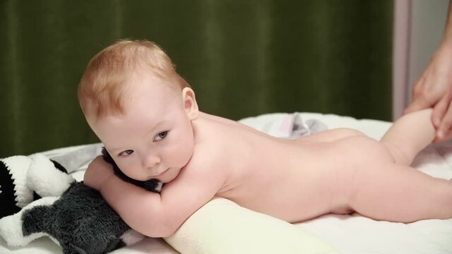 The Masseuse Gives A Leg Massage To A Happy Child (boy). The Baby Lies On His Belly, Holds A Soft Toy In His Hands. Baby Ticklish
