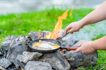 Tourist cooks breakfast on bonfire at morning - fries eggs and bacon