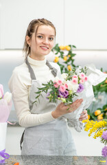Smiling florist wearing apron arranging a bouquet of beautiful colorful flowers inside her floral shop