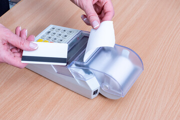 A hand holding a bank card above the cash register to pay for a purchase and a hand tearing off a check