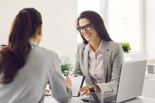 Friendly smiling human resources manager conducting job interview with applicant in office. Woman hired job seeker signing contract after successful negotiation with company HR employer in office