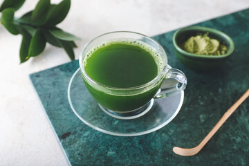 Cup of matcha tea, powder and chashaku on light background