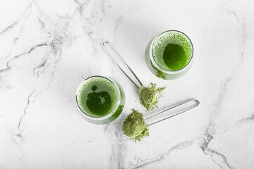 Glasses of matcha tea and powder on light background