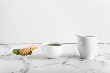 Cup of matcha tea, milk, powder and chasen on light background