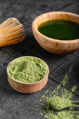 Bowl with matcha tea, powder and chasen on dark background