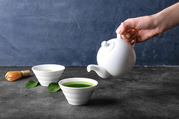 Woman pouring matcha tea from teapot into bowl on dark background
