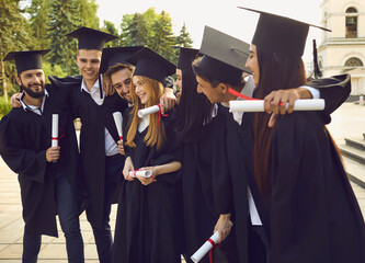 Group of smiling university graduates classmates in traditional bonets standing with diplomas,...