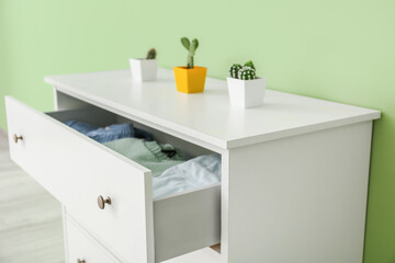 Modern chest of drawers and houseplants near color wall in room