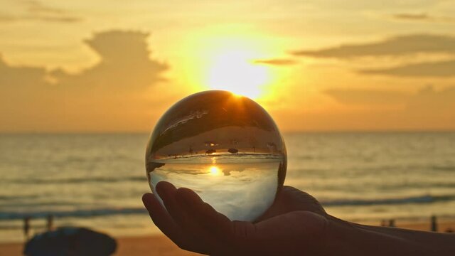 The hand held a crystal ball in sunset. The natural view of the sea is unconventional and beautiful. .A video for a unique and creative travel idea.4K clip