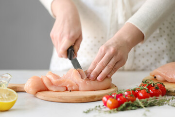 Obraz na płótnie Canvas Woman cutting raw chicken fillet on table