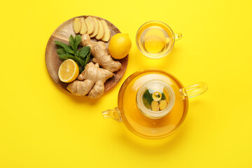 Teapot and cup of tea with ginger, mint and lemon on color background