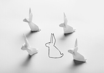 Drawn rabbit among made of origami on light background