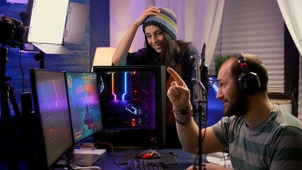 Side view of pro streamer couple performing online video games using powerful computer with multiple monitors. Player playing space shooter games during e-sport online tournament in streaming studio