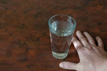 A glass with water and a man's hand on a red table.