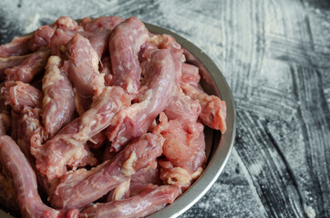Raw chicken necks in a metal bowl on a black with white backgrou