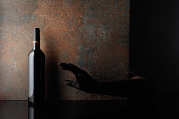 Woman hand in  glove reaches for a bottle of red wine.