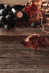 Bottle of red wine with grapes and dried vine on an old wooden table.