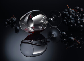 Blue grapes and wine glass with red wine on a black reflective background.