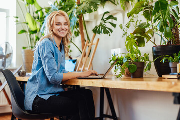 Joyful female business person works on her laptop in office with plants