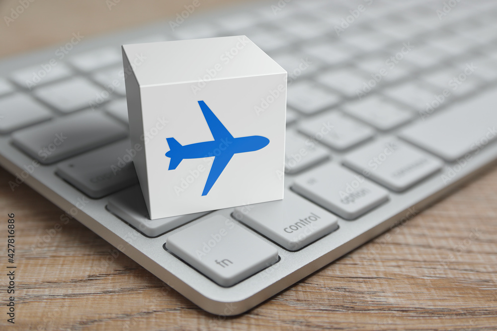 Poster airplane flat icon on white block cube with modern computer keyboard on wooden table, business trans