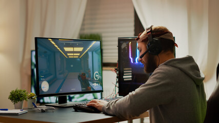 Cyber sport gamer wearing headphones playing first person shooter videogame participating in eSports tournament perforing at RGB prowerful personal computer. Pro cyber streaming gaming championship © DC Studio