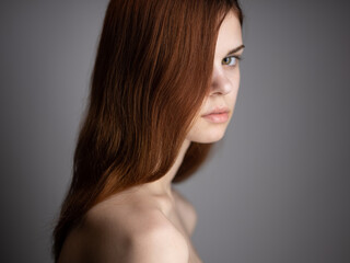 Portrait of a luxurious woman with red hair and bare shoulders on a gray background