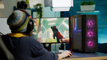 Back shot of pro streamer with headphone playing FPS videogame during esport competition using RGB powerful computer. Player sitting on gaming chair using streaming equipment late night in home studio © DC Studio